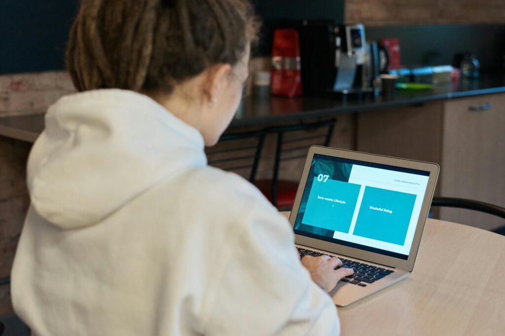 A woman in a white hoodie works on her laptop, focusing intently in a cozy cafe setting.